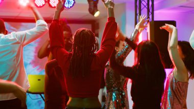 Gece kulübünde dans eden funky insanlar, sahnede DJ ve elektronik müzik için tezahürat yapıyorlar. Bir grup insan disko ışıkları ve ses paneliyle dans pistinde parti yapıyor ve zıplıyor. Üçayak atışı.