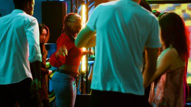 Çeşitli insanlar kulüpte elektronik müzik eşliğinde parti yapıyorlar ve DJ sahnede dans pistinde zıplıyorlar. Eğlenen ve eğlenen mutlu insanlar, disko ışıkları. Üçayak atışı.