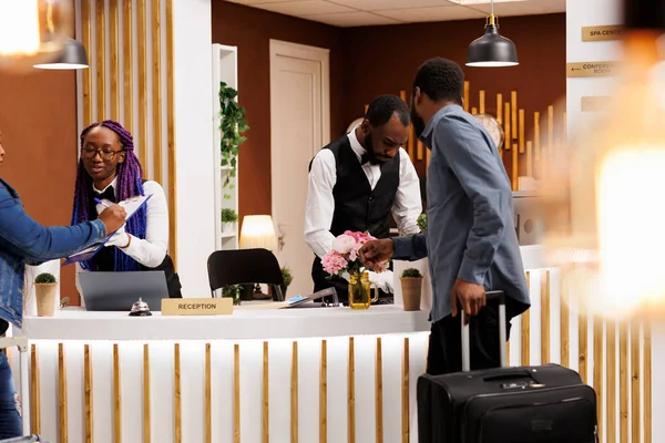 Two African American hotel receptionists man and woman assisting with booking rooms and check-in procedure, maintaining front desk. Customer service in hospitality industry
