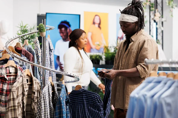 African american customer inspecting plaid shirt quality before buying in clothing mall. Fashion showroom man client choosing formal apparel and searching for label on sleeve
