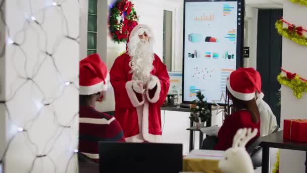 クリスマスシーズンの社員の前でプレゼンテーションをしているサンタクロースの格好のパブリックスピーカー Xmasのコワーカーは ミーティングルームで自分のキャリアを進める方法を学ぶ — ストック動画