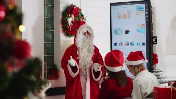 在圣诞季举行的团队会议上 经理扮成圣诞老人 在数字屏幕上展示公司明年的战略 与员工交谈的节日装饰办公室的领队 — 图库视频影像