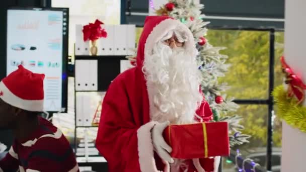 经理打扮成圣诞老人 在喜庆的装饰办公室里欢度节日 赠送礼物 拥抱员工 领队穿着服装给工人们带来惊喜的圣诞礼物 — 图库视频影像