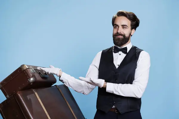 stock image Young bellboy presents directions in studio, point to left and right for marketing advertisement campaign. Professional hotel porter showing sideways ad over colored background.