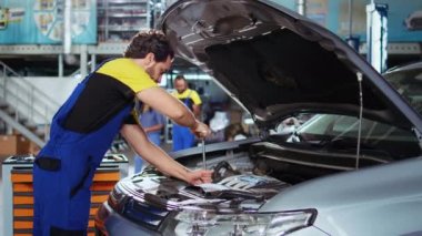 Araba servisindeki nitelikli servis elemanı, motoru değiştirdikten sonra cıvataları sıkmak için iş yerindeki banktan tork anahtarı seçiyor. Garaj çalışanı müşteri otomobilini tamir eder, yelkeni indirir.