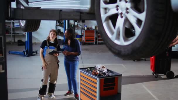 Doświadczony Mechanik Klient Stojący Pod Samochodem Garażu Przy Użyciu Laptopa — Wideo stockowe