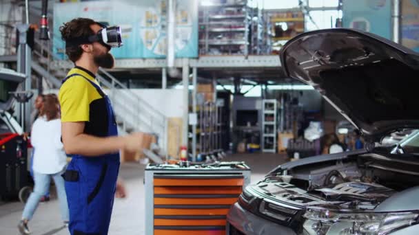 車のコンポーネントを可視化するために仮想現実ゴーグルを使用して自動修理ショップで訓練された技術者 バストされた車両で作業中に現代のVrヘッドセットを身に着けている男性 — ストック動画