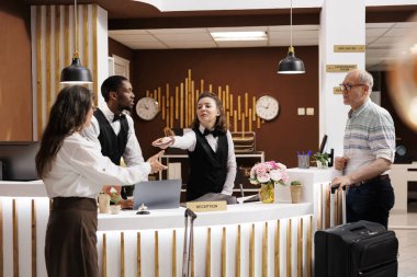 Rezervasyon onaylandıktan sonra kapıcıdan kimlik belgeleri alan turist kadın. Yaşlı çift otel resepsiyonunda bekliyor. Nazik çalışanlar giriş için onlara yardım ediyor..