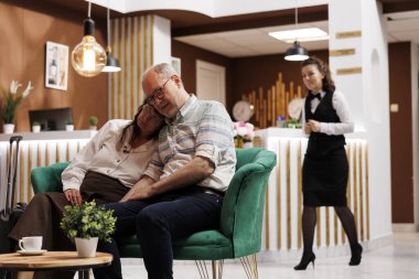 Yorgun yaşlı bir çift lüks otel lobisinde güzel koltuklarda uyukluyor. Uzun bir yolculuktan sonra, emekli kıdemli tatilciler kayıt için bekleme salonunda dinleniyorlardı. Dost canlısı otel çalışanları.