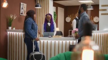 Otel kapıcısı beş yıldızlı otelde misafirleri karşılıyor, kayıt işlemlerinde kayıt işlemlerini gözden geçirmek için yolcularla konuşuyor. Afro-Amerikan halkı tatil gezisinde..
