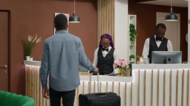 Resepsiyona giriş yapan, beş yıldızlı otele giriş yapan ve resepsiyona kayıt formlarını imzalayan biri var. Otel kapıcısı turistleri karşılıyor, harika hizmetler sunuyor..