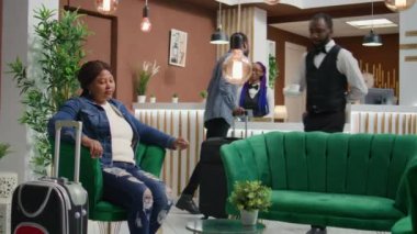Otel odasındaki kanepede oturan müşterilere kahve bardağı sağlayan otel çalışanları bardan içki alarak lüks hizmetler sunuyor. Afrikalı Amerikalı turist lobide içecek alıyor.