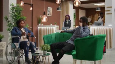 Tekerlekli sandalyede oturup maluliyet dostu otel lobisine girerken Afrikalı Amerikalı bir misafir adamla konuşuyor. Yurt dışına seyahat eden bir çift, seyyar turizm sektöründe azalma.