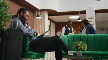 Otel misafiri tableti karıştırıyor ve oda rezervasyonunu beklerken kahvenin tadını çıkarıyor. Tatil yerindeki dinlenme odasında dinleniyor. Genç gezgin lüks kapıcı hizmetleri alıyor..