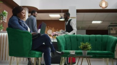 Otel müşterisi web sitesini onaylıyor, tatil köyünde konaklamayı bekliyor. Dosyaları incelemek ve sosyal medyayı kontrol etmek için dizüstü bilgisayar kullanan Afrikalı Amerikalı bir kadın..
