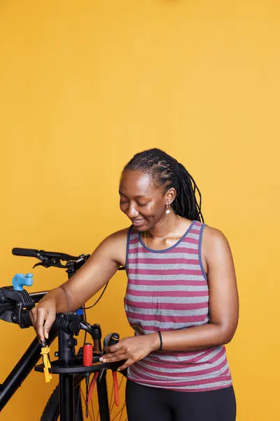 Photo showing healthy and athletic black woman holding professional tools and preparing for yearly bike maintenance. Youthful female placing specialized equipment on bicycle repair-stand.