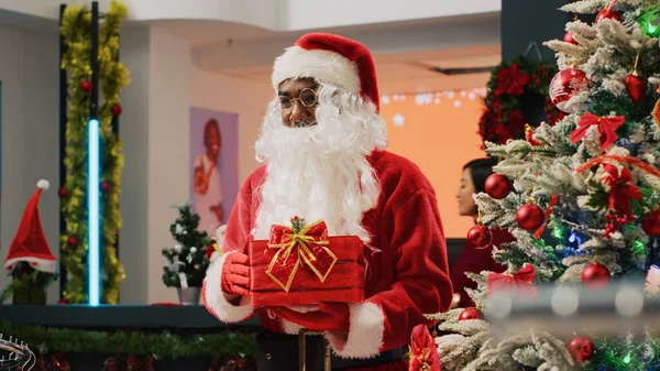 Xmasの高齢カップルは サンタクロースが収集ボックスとして機能するギフトを保持しているように 労働者にラッフルチケットを与える衣料品店を装飾しました クリスマスプロモーションイベントを主催する従業員 — ストック写真