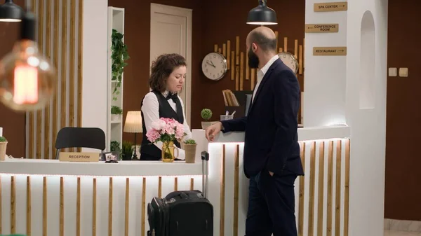 Concierge presenting hotel services to important guest with room reservation due to international conference attendance. Reception staff helping client to ensure pleasant business trip.