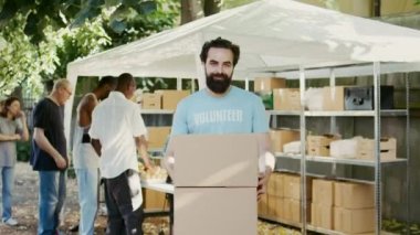 Aç ve evsizler için bozulmaz gıda ürünleri tutan nazik bir genç adam. Kameraya bakarken, beyaz bir erkek gönüllü bağış paketleri taşıyordu. El kamerasıyla..