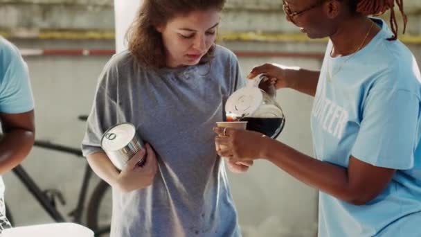 详细介绍了非洲裔美国女性志愿者为无家可归的高加索女性提供一杯咖啡的情况 野外食物库的友善黑人妇女与穷人分享营养 — 图库视频影像