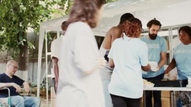 Kar amacı gütmeyen çok kültürlü bir ekip ihtiyacı olanlara ve imkanları az olanlara insani yardım dağıtıyor. Siyahi gönüllü kadın, yemek kampanyasında koltuk değnekli Afrikalı Amerikalıya yardım ediyor. El bilgisayarı.