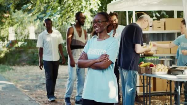 侧视图 黑人妇女戴着眼镜 双臂交叉 眼睛盯着相机 支持旨在减少饥饿和援助有需要者的非营利倡议的多族裔志愿人员 — 图库视频影像