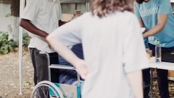 Starszy Pan Wózku Inwalidzkim Otrzymuje Darmowe Jedzenie Grupy Wielonarodowych Wolontariuszy — Wideo stockowe