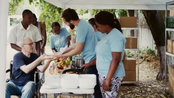 貧しい人々が新鮮な果物を含む無料の食べ物をホームレスの人々に与えるのを支援する慈善団体 ボランティアは 車椅子の障害者のための空腹を軽減するための支援を提供します — ストック動画