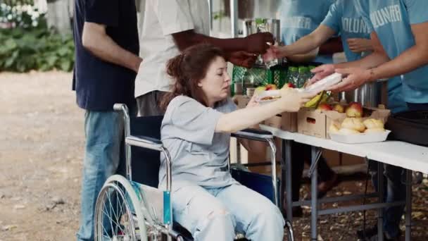 乐于助人的男子志愿帮助轮椅上的贫穷妇女 并为她们提供免费膳食 室外食品银行的慈善工作者向残废人和弱势群体提供人道主义援助 — 图库视频影像
