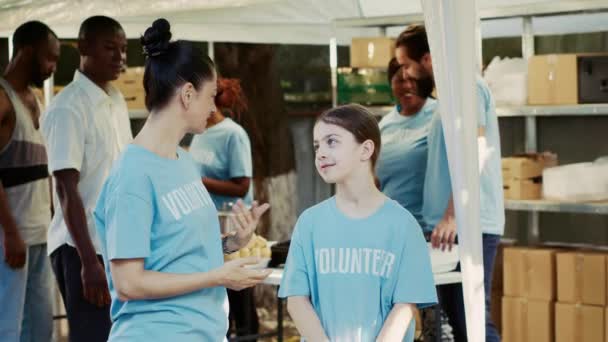 飢餓と戦うために外部の食糧銀行を支援する母親と娘の側面図 青色のボランティアTシャツの2人の白人女性は ホームレスの人々を支援するために準備されています — ストック動画