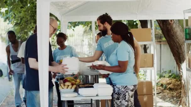 参加粮食分发活动的个人自愿向有需要的人慷慨地提供基本用品 身穿蓝色T恤衫 通过志愿工作提供饥饿救济援助的各种族人们 — 图库视频影像