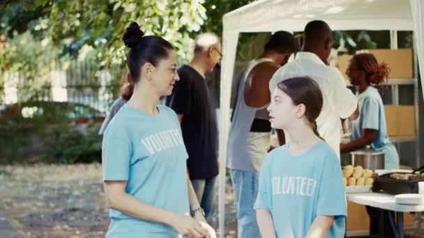参与户外食物银行饥饿救济计划的母亲和女儿的肖像照片 白种人志愿者身穿蓝色T恤 看着镜头 随时准备帮助有需要的人 三脚架射击 — 图库视频影像