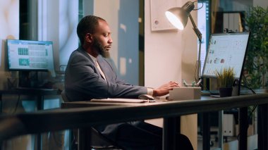 Kayıt memuru, gece vardiyası sırasında uygun olmayan değerler için çevrimiçi şirket belgelerini kontrol etmeye odaklandı. Ofisteki çalışanlar evrak işlerine dikkat ediyor, doğruluğunu teyit ediyorlar.