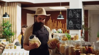 Mutlu sıfır atık süpermarket sahibinin portresi iklim etkisini azaltmak için geri dönüşümlü cam kaplar kullanıyor. Neşeli mahallenin dükkan işletmecisi, malları düzenliyor.