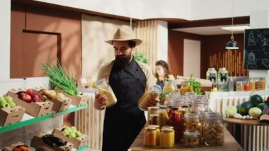 Gülümseyen bir satıcının portresi sürdürülebilir sıfır atık süpermarket raflarına zımba ekliyor. Mutlu satıcı tekrar kullanılabilir kavanozlarda organik gıda stokluyor.