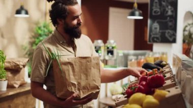 Sıfır atık süpermarketindeki vejetaryen adam biyolojik sebze alırken biyolojik çözünebilir kağıt torba kullanıyor. Tek kullanımlık plastik politikası olmayan karbon nötr yerel bakkal müşterisi