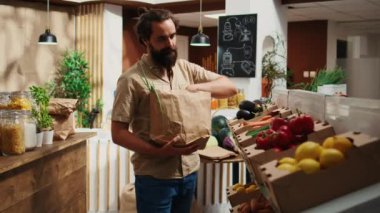 Dolly, sıfır atık süpermarketinde, sebze alırken kirletici olmayan kağıt torba kullanan bir adamı yakından çekiyor. Karbondioksit salınımını azaltmak için tek kullanımlık plastik politikası kullanmayan yerel bir dükkan müşterisi
