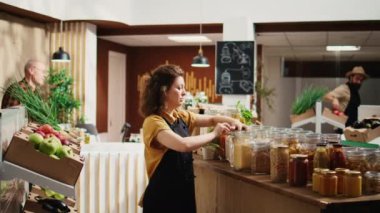 Sıfır atık organik gıda süpermarketinde çalışan gülümseyen kadın portresi raflara zımba ekliyor. Neşeli çalışan, yerel marketi yeniden kullanılabilir kavanozlarda toplu ürünlerle dolduruyor.