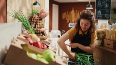 Çalışkan çevre dostu market çalışanı rafları taze meyve ve sebzelerle dolduruyor. Mahalledeki süpermarket sahibi sergilenen organik tarım ürünleri ekliyor