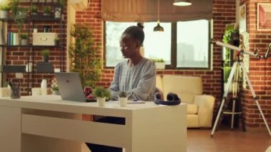 Ev tabanlı Afro-Amerikan bağımsız işçi güne online iş için ev işlerini tamamlamakla başlıyor. E- postalara cevap vermek için bilgisayarını kullanan kadın telesekreter ve kişisel blog yazarı.