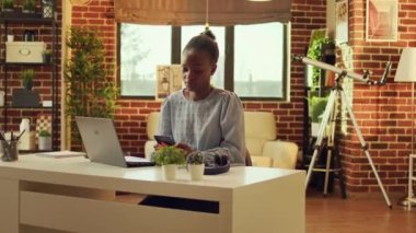Günlük işleri ve ağ bağlantılarını çözmeden önce web sayfasında serbest çalışan ve sosyal medya uygulamalarını kontrol eden bir kadın. Afrika kökenli Amerikalı tele-işçi gün batımında masada oturuyor..