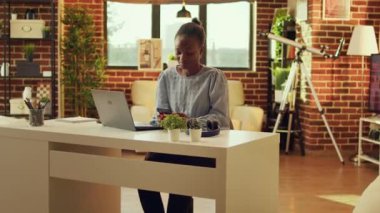 Kadın tele-işçi, günlük serbest işlere ve ağ bağlantılarına başlamadan önce web sayfasını karıştırıyor ve sosyal medyayı kontrol ediyor. Günbatımında masasında oturan Afrikalı Amerikalı serbest çalışan kişi..