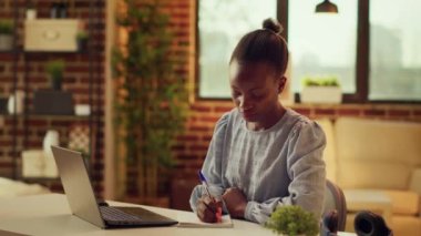 Freelancer iş hakkında notlar alıyor, masadaki uzak iş verimliliğine yardımcı olmak için dizüstü bilgisayar planlayıcısı kullanıyor. Afrika kökenli Amerikalı kadın fikirleri ev ofisi olarak yazıyor..