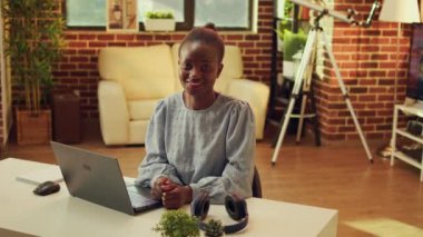 Masadaki Afrikalı Amerikalı tele-işçi gün batımında güzel aydınlatılmış bir odada online görevler üzerinde çalışıyor. Freelancer evde uzaktan çalışıyor, blog yazıyor ve e-posta gönderiyor. Çoklu Görev.