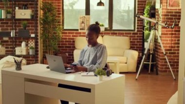 Heyecanlı kadın evde online alışveriş yapıyor, dizüstü bilgisayarına kredi kartı bilgilerini dikkatlice yazıyor. Afrikalı Amerikalı ödemeyi web sitesine ekliyor, gün batımında sıcak bir yerde oturuyor..