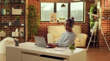 Mutlu işçi müzik dinler, evdeki laptopta bilgi yazar. Afrikalı Amerikalı serbest yazar online kariyer yaratıyor, uzaktan işten keyif alırken kulaklıklardan şarkılar söylüyor..
