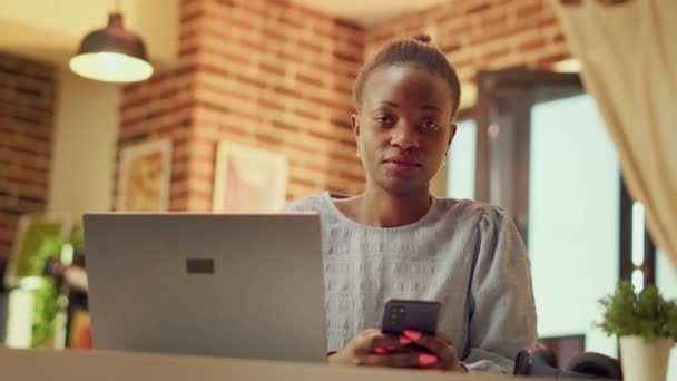 日落时 非裔美国自由职业者在家里的办公室里用电话 看在线社交媒体上的帖子 从事自由职业 多任务工作的妇女远程工作者开发人员 手持射击 — 图库视频影像