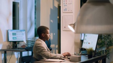 Afrika kökenli Amerikalı yönetici, çalışanlardan modern ofiste gece vardiyası sırasında şirket projelerinin nasıl ilerlediğini göstermelerini istedi. İdari yönetici iş yerindeki belgeleri çapraz kontrol ediyor