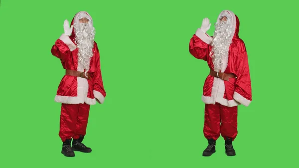 友好的人物形象在镜头前挥手致意 穿着传统节日服装传播圣诞精神 打扮成圣诞老人的年轻人打招呼 绿屏背景 — 图库照片