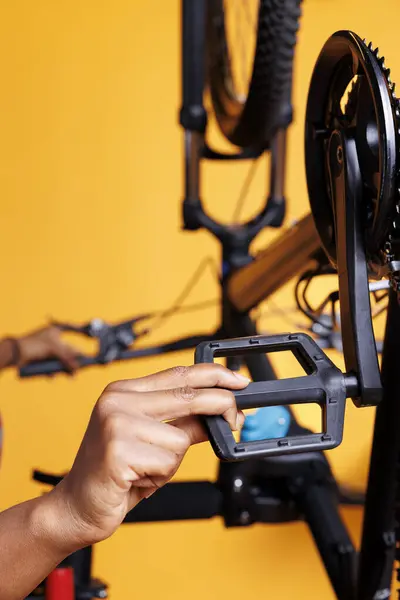 Close-up shot of african american individual fixing a bicycle and doing routine maintenance. Detailed image showcasing a pair of hands repairing and adjusting bike pedals for recreational cycling.